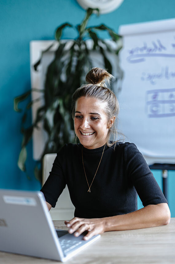 Teilnehmerin des Change Management Online Trainings sitzt am Laptop und grinst | Kraus & Partner - Transformation Experts