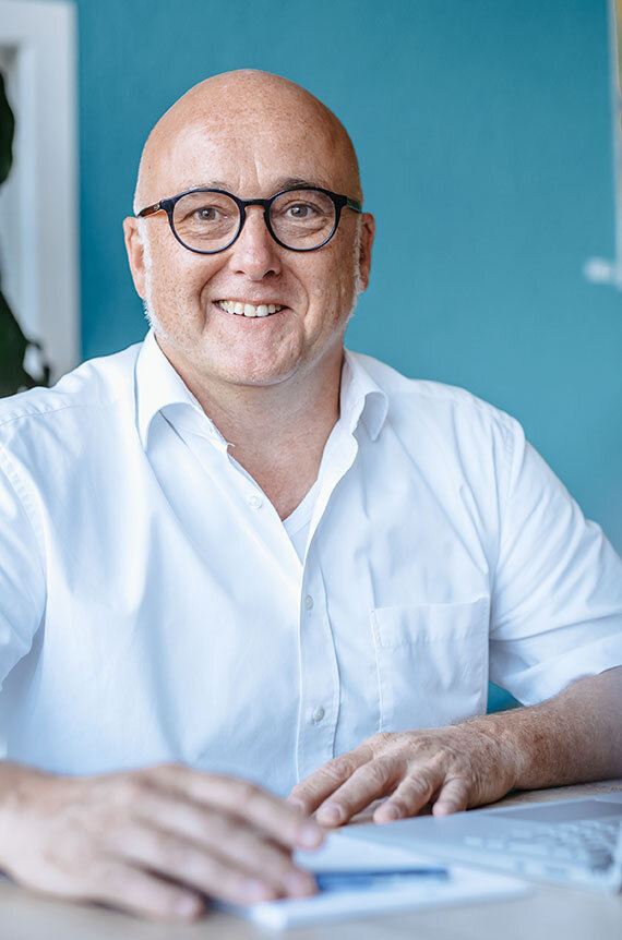 Change Management-Trainer Stefan Bald sitzt am Laptop und schaut lächelnd in die Kamera | Kraus & Partner - Transformation Experts