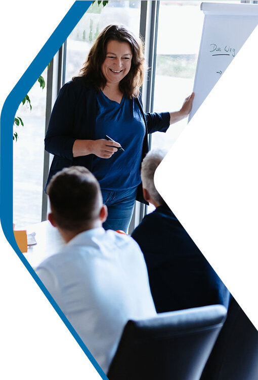 Transformationsexpertin Daniela steht lachend am Flipchart vor einer Gruppe von Menschen | Kraus & Partner - Transformation Experts
